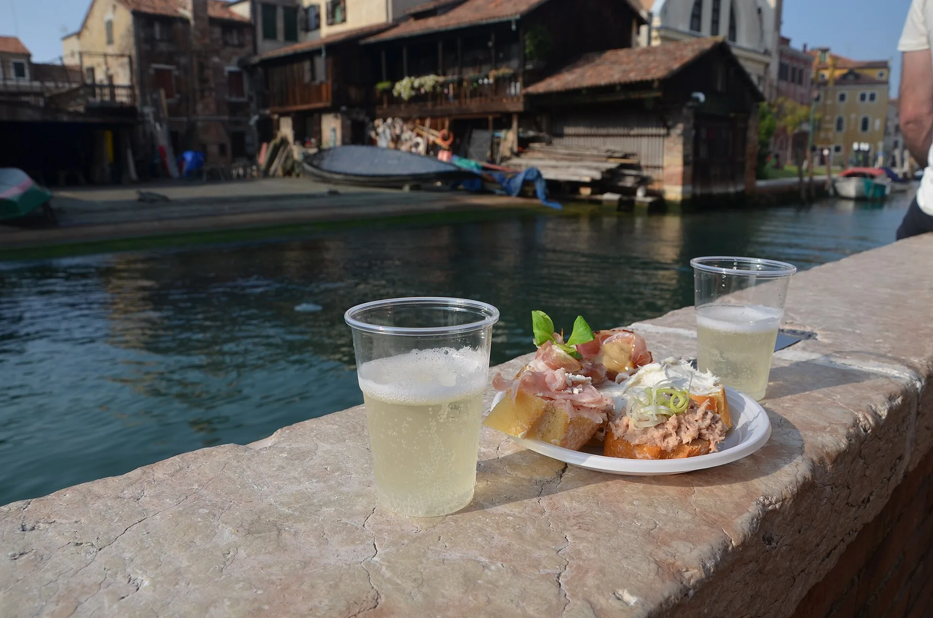 Cicchetti veneziani e un bicchiere di prosecco su un muretto affacciato su un canale